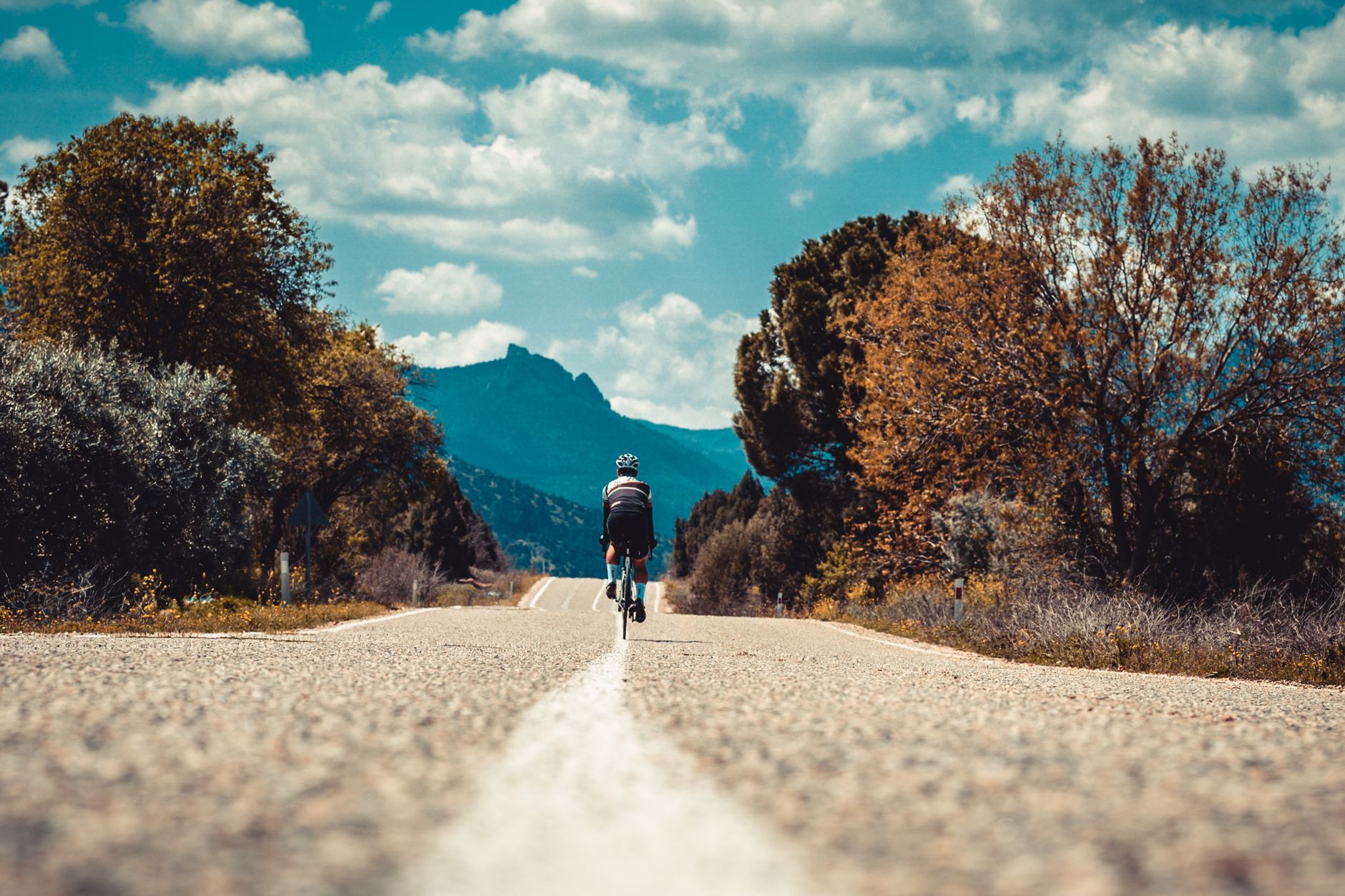 Ciclista pedaleando por una carretera rural con montañas al fondo