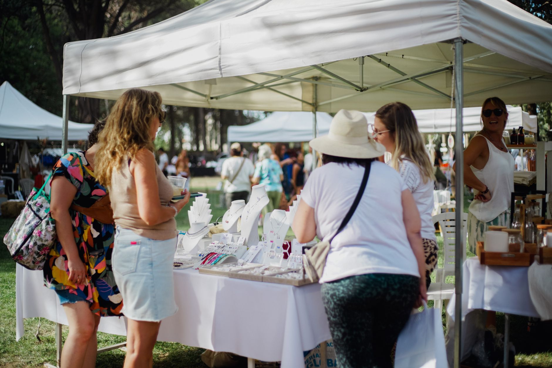 Visitantes recorren puestos de joyería en un mercado artesano al aire libre en un día soleado