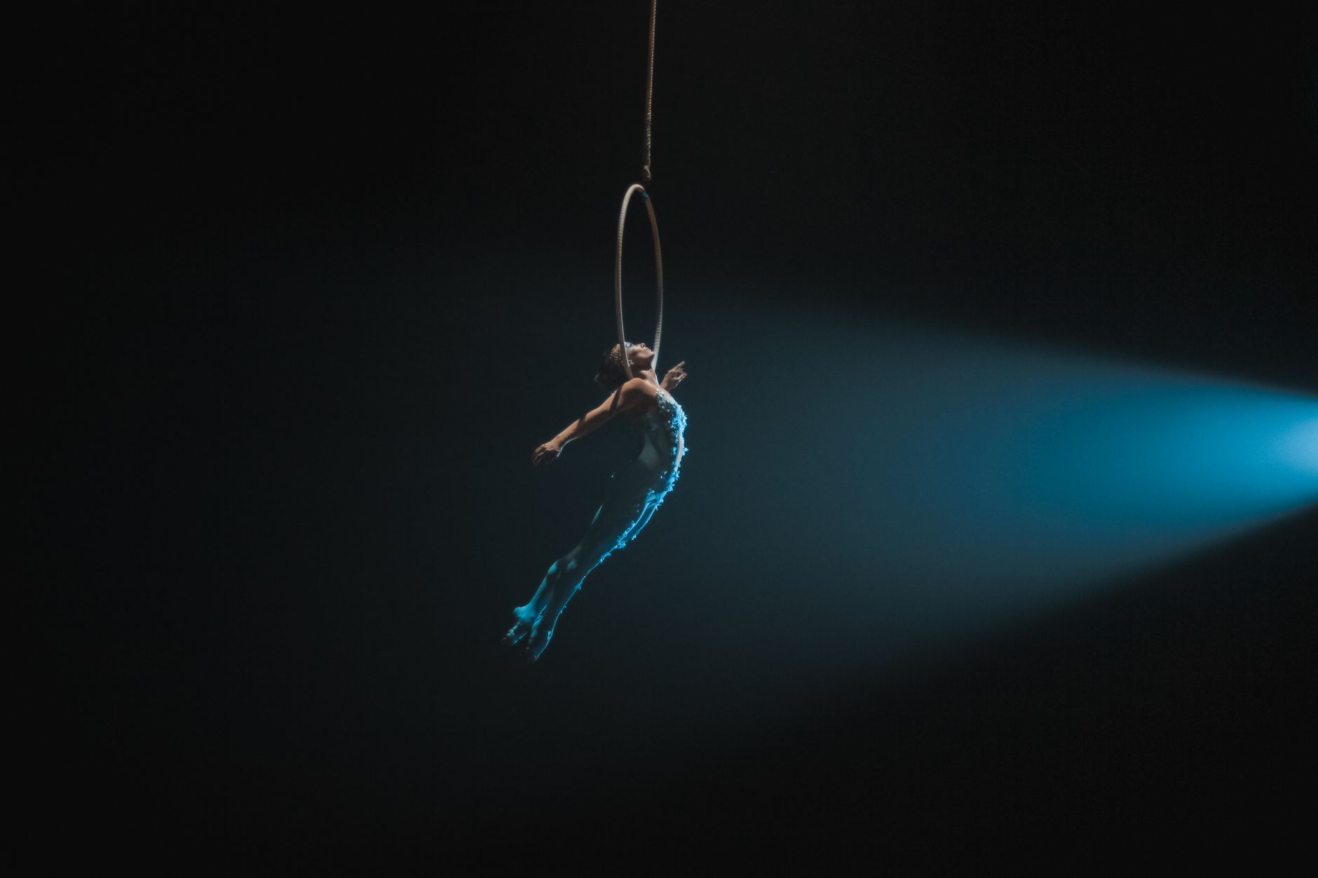 Artista aérea actuando en un aro bajo un foco de luz azul